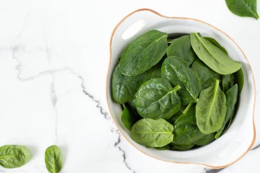 Beyaz mermer arka planda bir kasede taze ıspanak yaprakları. Üst Manzara. Boşluğu kopyala.