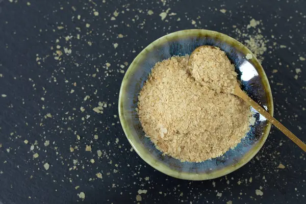 Koyu arka planda kaşıkla kasede besin değeri olan maya taneleri. Üst Manzara. Vejetaryen peyniri yerine yiyecek..