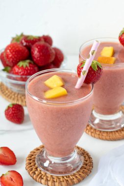 Beyaz mutfak masasında bir bardakta çilekli mango smoothie. Sağlıklı yaz karışımı..