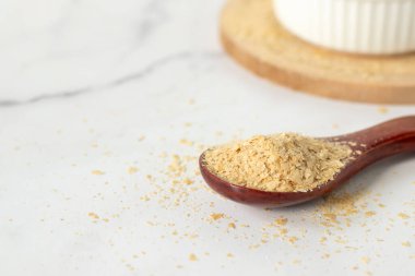 Beyaz mutfak masasında tahta kaşıkta besin değeri yüksek maya taneleri. Yakın plan. Boşluğu kopyala.