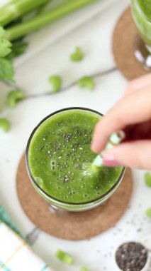 Yeşil kereviz sosunu bir bardakta samanla karıştırıyorum. Dikey video. Kahvaltıda sağlıklı vejetaryen karışımı..