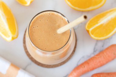 Portakal ve havuç püresi beyaz mermer masada bir bardakta. Üst Manzara. Sağlıklı harmanlanmış kahvaltı içeceği.