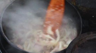 Ortaçağ tarihi canlandırması. Tahta kaşık soğan çorbası, baklagiller ve buhar çıkaran et karışımı. Dökme demir bir kazanda yemek.