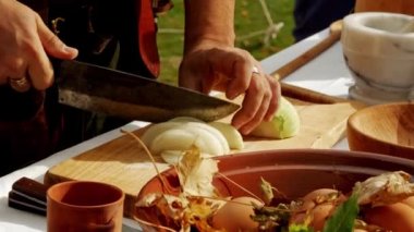 Ortaçağ tarihinin yeniden canlandırması. Ortaçağ yemek kampında bir kesme tahtasında beyaz soğan doğrama, kırsal alanda yemek pişirme sahnesi.