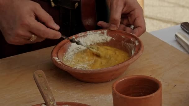 中世纪的再现 穿着中世纪服装的人把一些鸡蛋和面粉放进碗里准备一道菜 — 图库视频影像