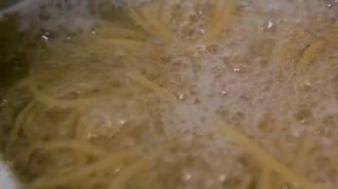Geleneksel İtalyan yemekleri olan spagettiyi pişirmek için içinde kaynar su bulunan metal bir tencerenin üstünden yakın çekim.