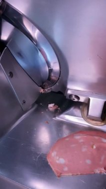 Mortadella dilimlerini kesen elektrikli bir doğrama makinesinin yakın plan çekimi. İtalyan usulü domuz eti. İtalyan mutfağı, tipik ürünler ve İtalyan pişirilmiş etleri.