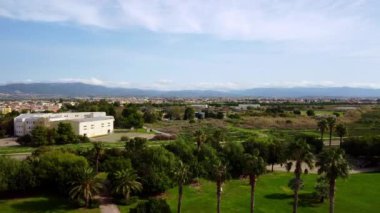 Okul ve büyük yeşil çimlerin olduğu panoramik bir şehir parkının 4k 'lik insansız hava aracı görüntüsü ilerliyor. İnsansız hava aracı videosu şehri ve doğayı parkediyor