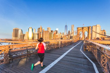 Brooklyn Köprüsü 'nün arka planında bir koşucu ve New York şehrinde gün doğumunda mavi gökyüzü. 