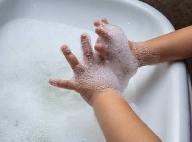 Çocuk banyo lavabosunda köpük dolu elleri yıkıyor..