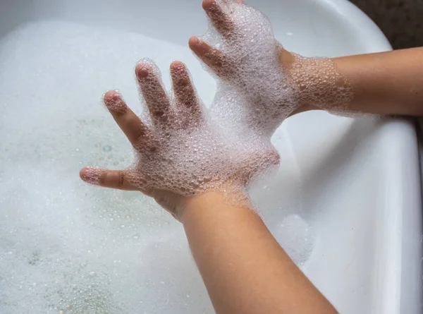 Child washing hand full of foam in bathroom sink.