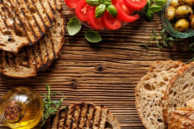 Izgara ekmek dilimleri ve çeşitli geleneksel ürünler; yeşil zeytin, zeytin yağı, domates ve fotokopi alanı olan ahşap bir masada taze otlar. Akdeniz mezeleri.