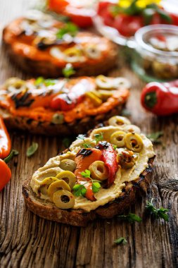 Kızarmış geleneksel ekmekli sandviçin yanına humus, ızgara biber ve ahşap bir tahtanın üzerine taze maydanoz serpiştirilmiş zeytin serpiştirilmiş ekmeklerini yakın plan çek.