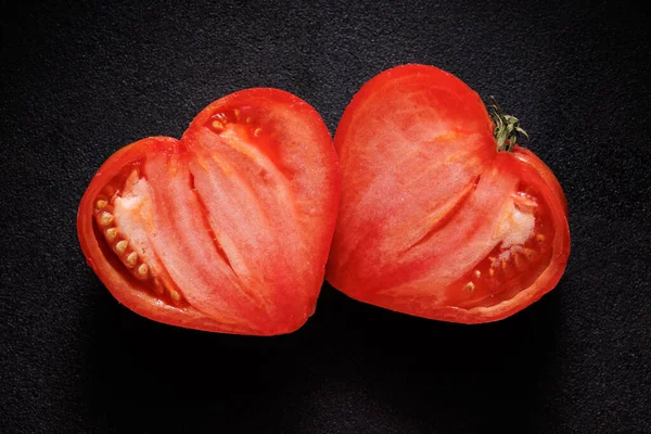 Heart-shaped tomato cut in half on a black background. Valentine\'s tomato