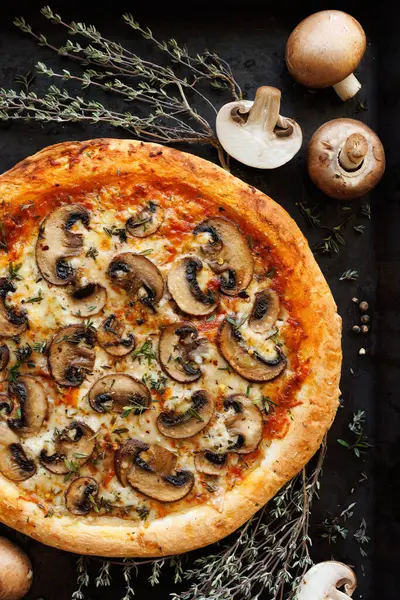 Mushroom pizza with the addition of sliced brown mushrooms, champignons and herbs on a black background, close-up