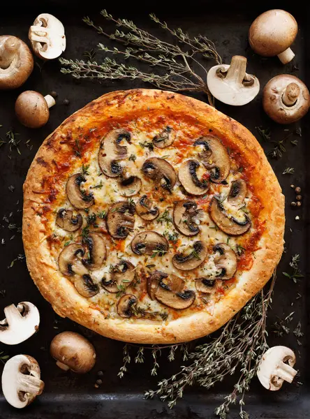 Mushroom pizza with the addition of sliced brown mushrooms, champignons and herbs on a black background, top view