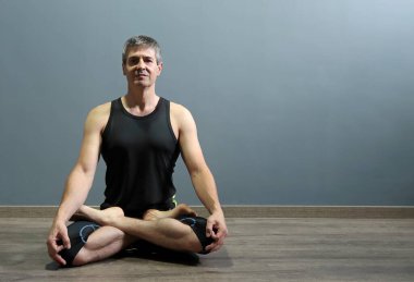 Athletic and handsome mature man practicing yoga in the asana pasmasana or lotus position