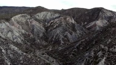 İspanya 'nın güneyinde sarp bir bölgenin havadan çekilmiş videosu, bir çok vadi var, yeryüzünün farklı gölgeleri var, çalılar var, gökyüzü bulutlu.