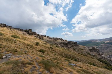 Sierra Nevada dağının yamacında kaya oluşumları, kayalar gri renkli, çalılar var, gökyüzünde bulutlar var.