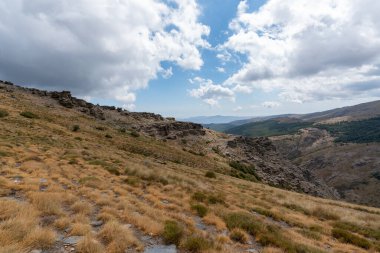 Sierra Nevada dağının yamacında kaya oluşumları, kayalar gri renkli, çalılar var, gökyüzünde bulutlar var.