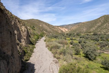 Granada 'nın güneyindeki dağların arasındaki vadide kurumuş bir nehir var, zeytin ağaçları var, çalılar var, gökyüzünde bulutlar var.