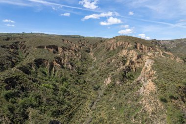 Granada 'nın güneyindeki dağlık arazi, birkaç vadi var, arazi aşınmış, ağaçlar ve çalılar var, gökyüzünde bulutlar var.