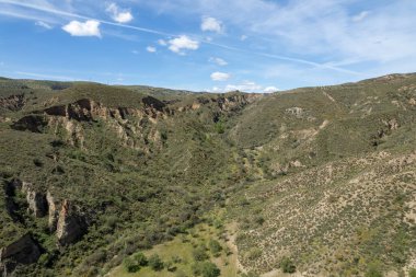 Granada 'nın güneyindeki dağlık arazi, birkaç vadi var, arazi aşınmış, ağaçlar ve çalılar var, gökyüzünde bulutlar var.