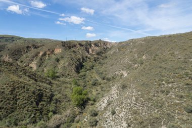 Granada 'nın güneyindeki dağlık arazi, birkaç vadi var, arazi aşınmış, ağaçlar ve çalılar var, gökyüzünde bulutlar var.