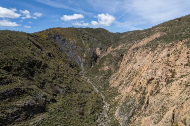 Granada 'nın güneyindeki dağlık arazide ağaçlar ve çalılar var, bir vadi var, gökyüzünde bulutlar var.