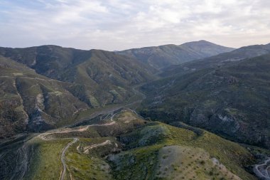 Granada 'nın (İspanya) güneyindeki dağlık arazide çalılar ve ağaçlar var, gökyüzünde bulutlar var.