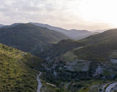 Granada 'nın (İspanya) güneyindeki dağlık arazide çalılar ve ağaçlar var, gökyüzünde bulutlar var.