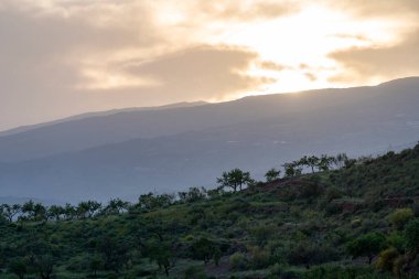 Granada 'nın güneyindeki dağlık arazi badem ağaçları yetiştiriliyor, çalılar var, gökyüzü bulutlu ve güneş batıyor.