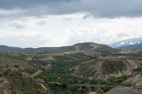 Granada 'nın güneyindeki dağlık bölgede bir yol geçiyor ve bir köprü var, zeytin ağaçları var, gökyüzünde bulutlar var.