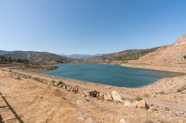 Endülüs 'ün güneyindeki Beninar Barajı, çalıları ve ağaçları olan bir dağ bölgesi. Gökyüzü açık.