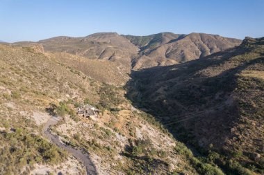 Granada 'nın güneyindeki dağlarda günbatımı, birkaç çiftlik evi, dağların arasından geçen bir nehir, dağlarda çalılar ve ağaçlar var, gökyüzü açık.