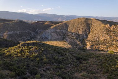 Granada 'nın güneyinde dağlar, birkaç vadi var, çalılar ve ağaçlar var, birkaç çiftlik evi var, gökyüzü açık.