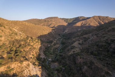 Granada 'nın güneyindeki dağlarda gün batımı, dağlar arasında bir nehri geçer, çalılar ve ağaçlar vardır, gökyüzü açıktır