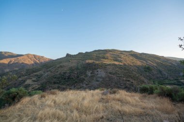 Granada 'nın güneyinde dağlar, kayalar, çalılar ve ağaçlar var, gökyüzü açık.
