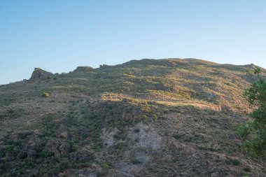 Granada 'nın güneyinde dağlar, kayalar, çalılar ve ağaçlar var, gökyüzü açık.