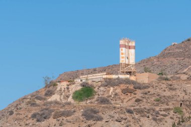 Endülüs 'ün güneyindeki eski beton fabrikası. Kırmızı çizgili birkaç silo var. Ağaçları ve çalıları olan dik bir alan.