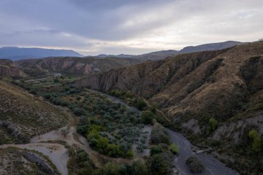 Granada 'nın güneyindeki dağlık bölgede, kuru bir nehir var, dağlarda ağaçlar ve çalılar var, gökyüzü bulutlu.