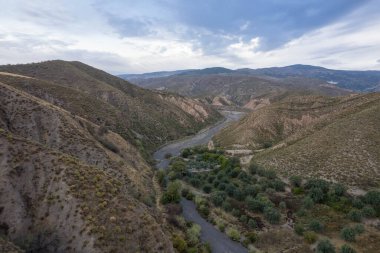 Granada 'nın güneyindeki dağlık bölgede, kuru bir nehir var, dağlarda ağaçlar ve çalılar var, gökyüzü bulutlu.