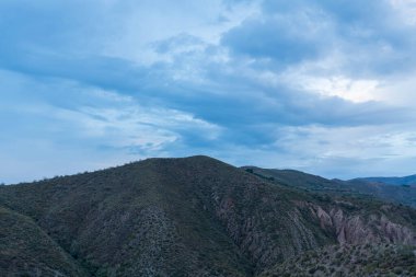 Granada 'nın güneyinde şafak vakti, bir dağ bölgesi, dağda bitki örtüsü var, gökyüzü bulutlu.