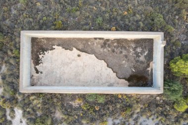 Su depolamak için eski bir inşaatın tepeden çekilmiş fotoğrafı. İnşaat betondan yapılmış. Etrafında çalılar var.
