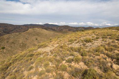 İspanya 'nın güneyindeki dağlık arazi, dağın yamaçlarında vadiler var, dağlar çalılarla kaplı, gökyüzü bulutlu.
