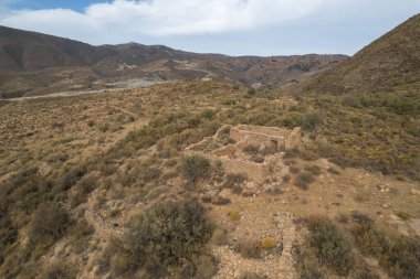 Güney Granada dağlarında harabe bir çiftlik evi, çiftlik evi taştan yapılmış, ağaçlar ve çalılar var, gökyüzü bulutlu.