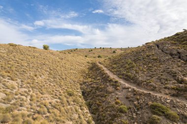 Granada 'nın güneyinde dağlık bir arazi, dağlık alanda toprak bir yol var, çalılar ve ağaçlar var, bir vadi var ve gökyüzünde bulutlar var.
