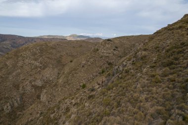 Güney İspanya 'da sarp dağlar, yamaçlarda çalılar ve kayalar, birçok vadi var ve gökyüzünde bulutlar var.