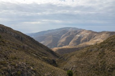 İspanya 'nın güneyindeki dağlık arazi, dağın yamaçlarında vadiler var, dağlar çalılarla kaplı, gökyüzü bulutlu.