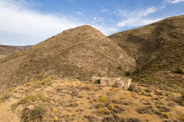 Güney Granada dağlarında harabe bir çiftlik evi, çiftlik evi taştan yapılmış, ağaçlar ve çalılar var, gökyüzü bulutlu.